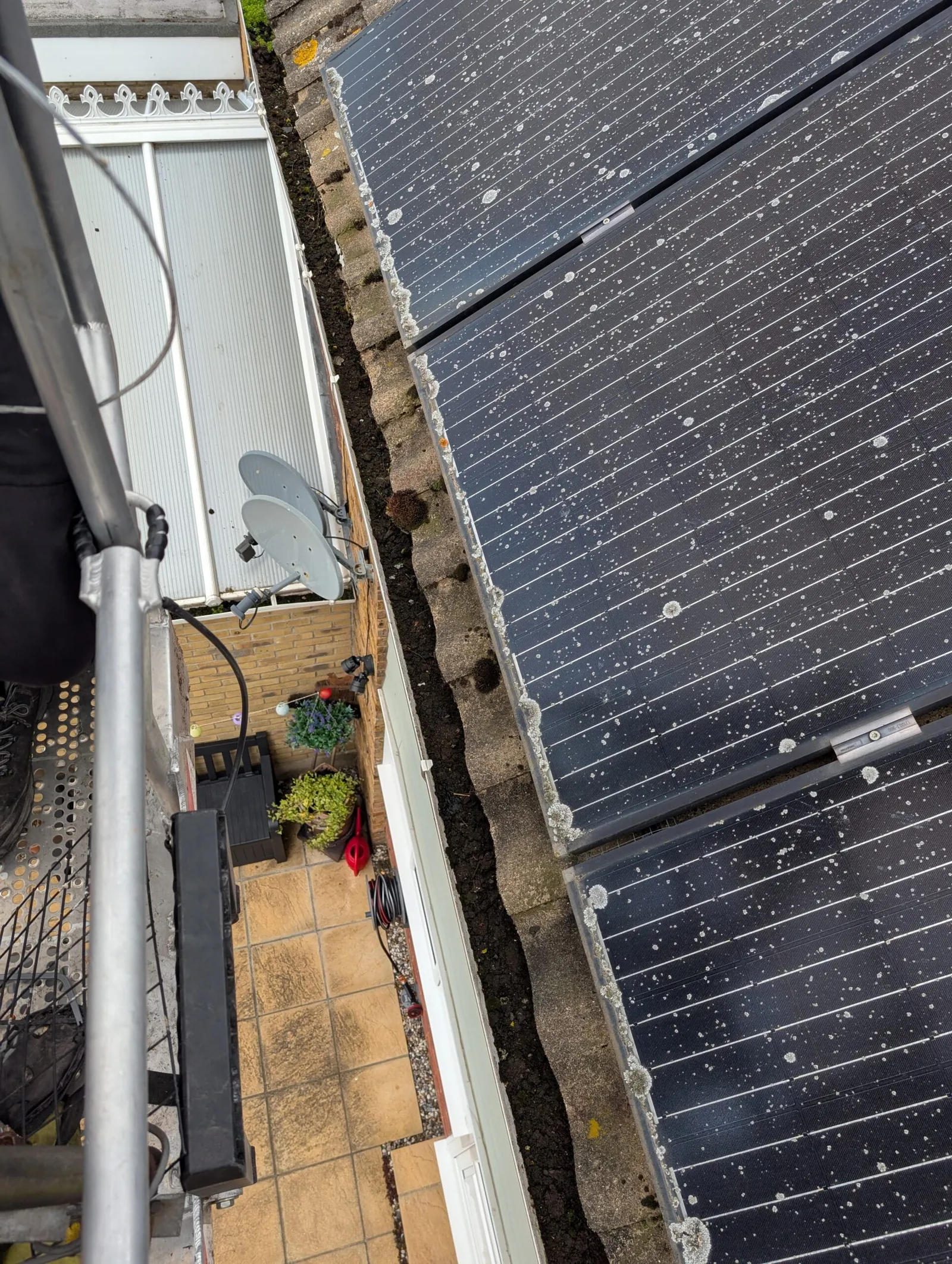 Blocked gutter packed with silt and moss running alongside a rooftop solar array