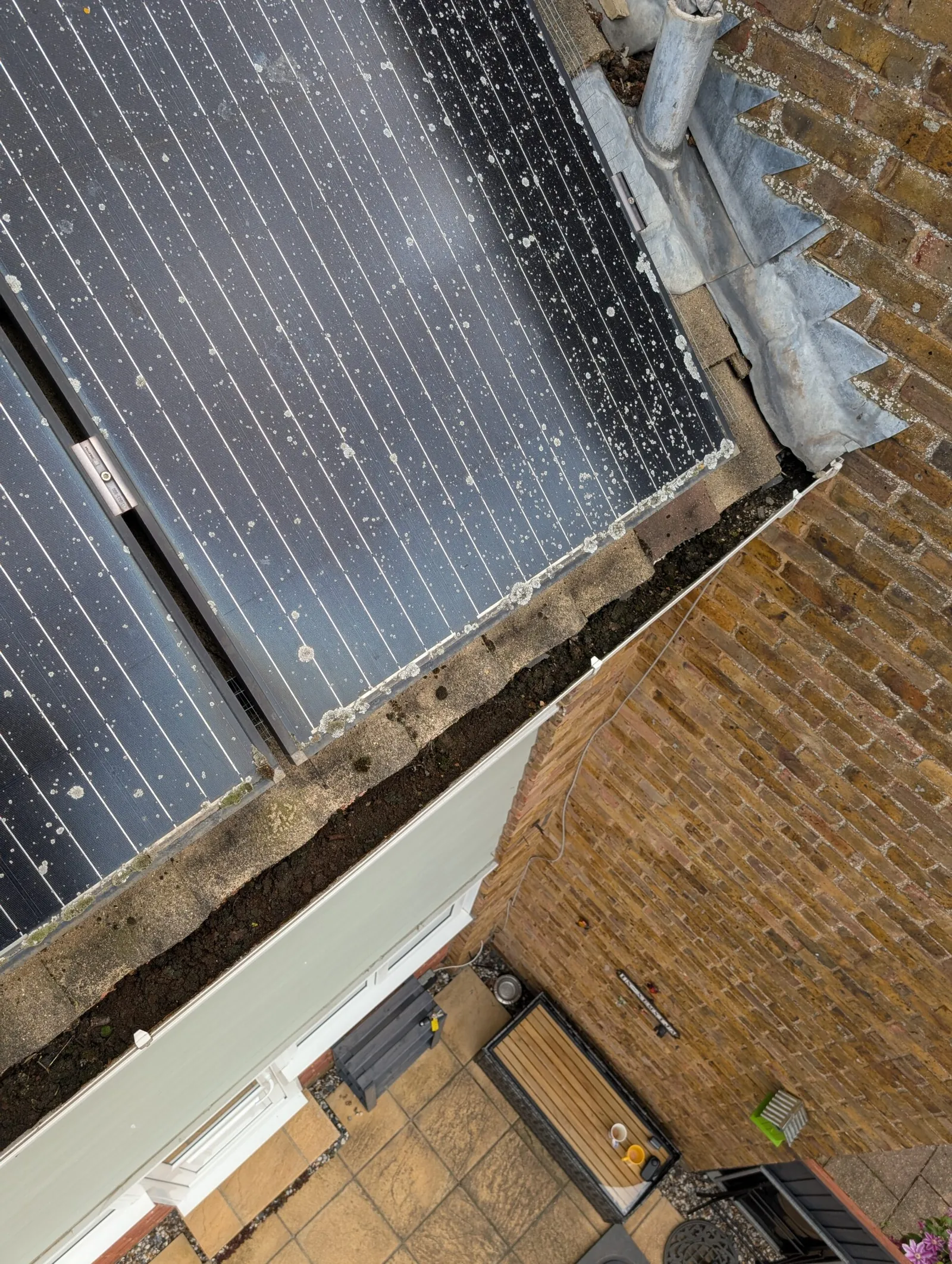 Gutter full of debris beside a solar array, with water tracking down into the roof valley