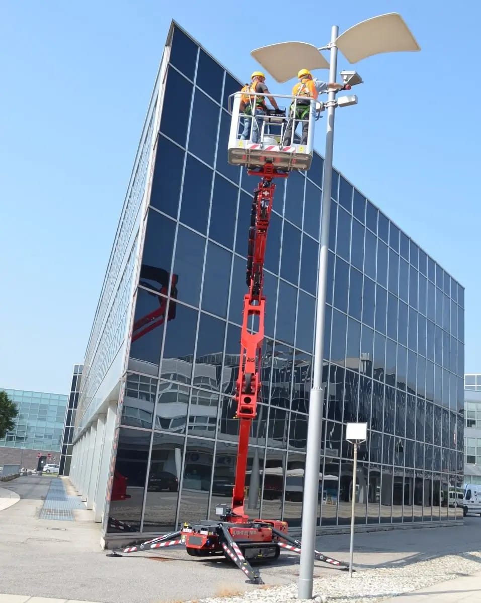 Two LADS operatives working from a tracked spider lift platform against a glass-clad office elevation