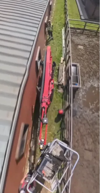 Machine threaded along the narrow gap between a building and a boundary fence, viewed from the platform