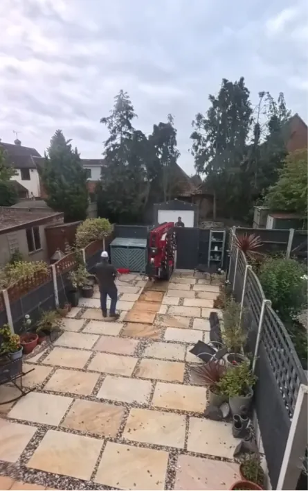 Operator walking the tracked lift across a paved rear garden to reach the back of the house