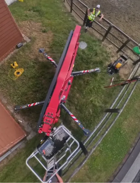 Spider lift set up on a narrow strip of ground between a farm building and a paddock fence